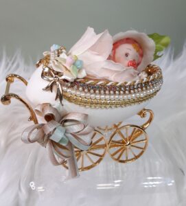 An egg hollowed out with wheels resembling a carriage with a baby inside.