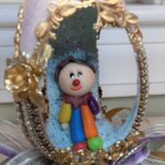 Jeweled egg with an open, glittered interior with a clown doll inside.