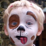 Blonde child with white, black, and brown face paint resembling a dog.