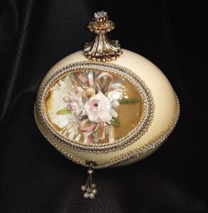 Goose egg with gold top, jeweled necklace, with a flowery image in the middle.